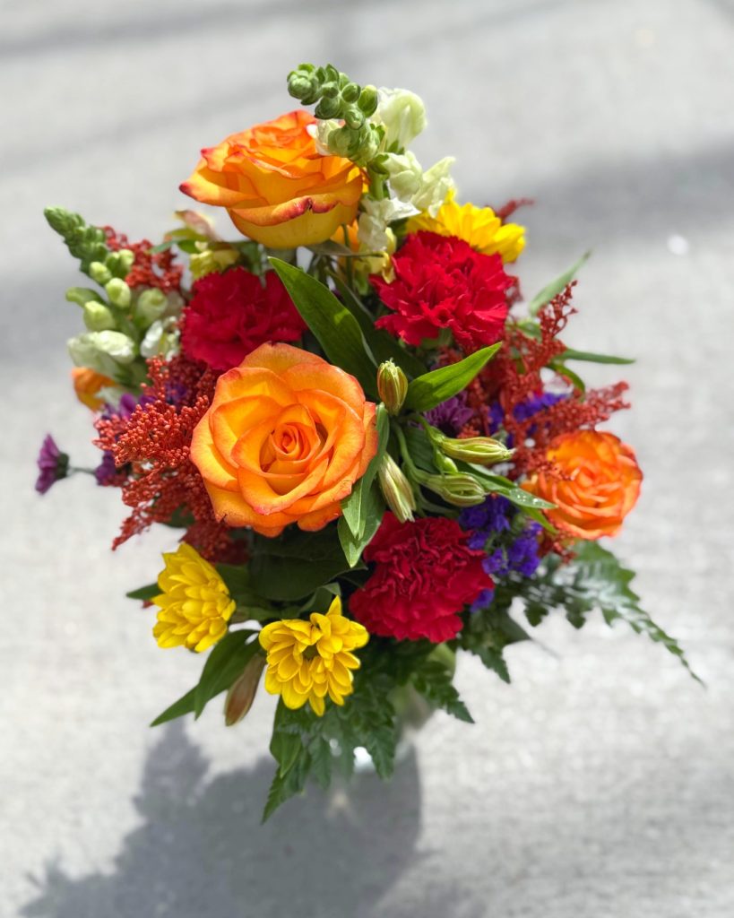 A vibrant bouquet of flowers in a glass vase, featuring saturated tones of orange, red, yellow, and green